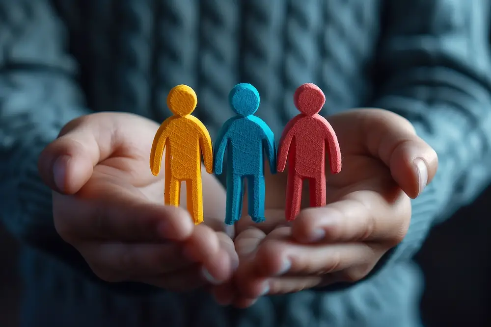 Cupped hands holding three wooden figures, showing security
